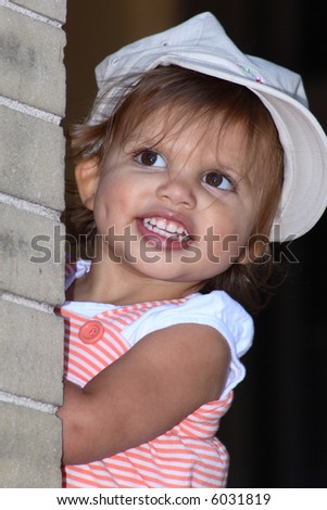 A toddler girl with a dimple on one cheek playing peek-a-boo