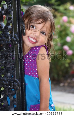 toddler posing in a rose garden by an iron gate with a cute big smile