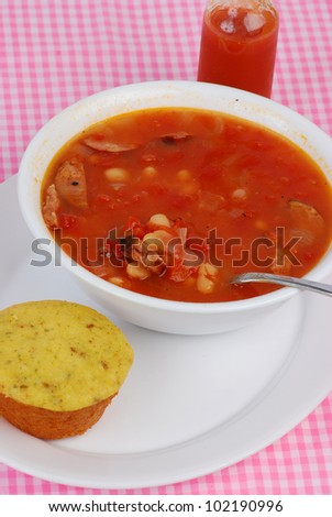 Bowl of spicy Cajun sausage soup with Jalapeno cornbread muffin and bottle of hot sauce.