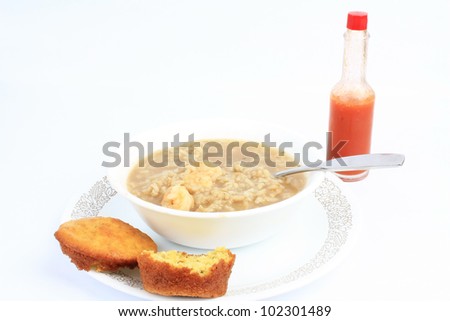 Bowl of spicy cajun shrimp gumbo with cornbread muffin and bottle or red hot sauce.
