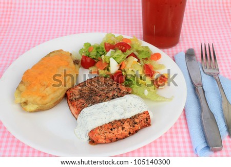 Large Salmon Steak coated with spices and grilled to perfection served with special tartar sauce, twice-baked potato and mixed salad and sweet iced tea.  Pink gingham place mat as background.