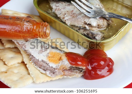 Sardines on saltine crackers with ketchup and hot sauce being poured from bottle.