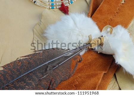 Display of leather, feathers and beaded Native American jewelry and crafts material -- buckskin, white rabbit fur along with choker necklace, feather headdress and rawhide thongs.