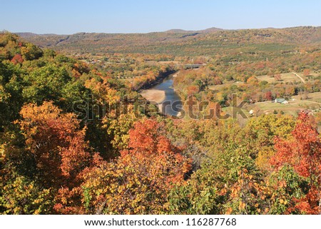 White River running through valley of farming village in Ozark Mountains of Northern Arkansas fronted by colorful Autumn leave in October.