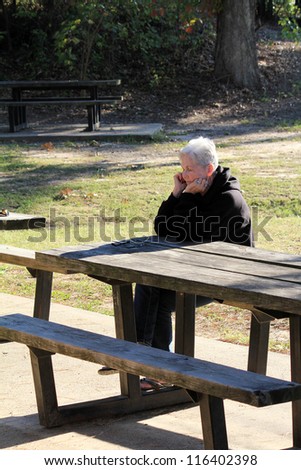 Long shadows and strong back light add interest to image of silver-haired senior woman relaxing at park bench in evening warmth.