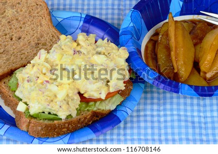 Tuna Salad Sandwich on whole grain bread with sliced tomato and lettuce served with sliced apple caramelized in cinnamon syrup on blue paper plate and bowl.