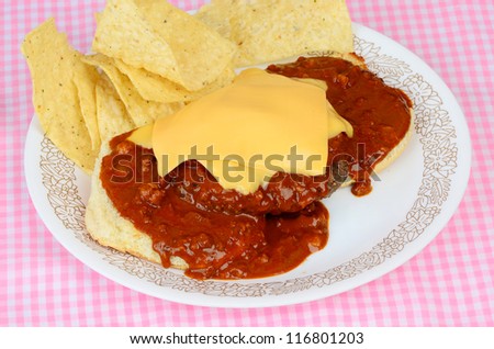 Chile poured over open face hamburger with cheese melting on the spicy hot chile.  Served with chips on pink gingham place mat.