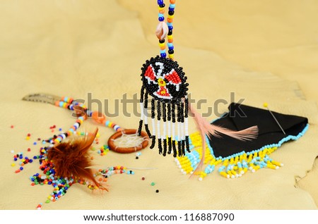 Beaded Native American dream catcher and medicine bag spread over buckskin background with focus on  Thunderbird Medallion.  Colorful beading equipment add interest.