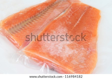 Frozen salmon steaks still in plastic wrap thawing on white background in preparation for cooking.
