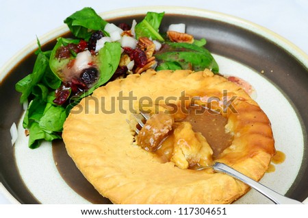 Steaming hot beef pot pie in golden brown crust with spinach and cranberry salad on simple design plate.