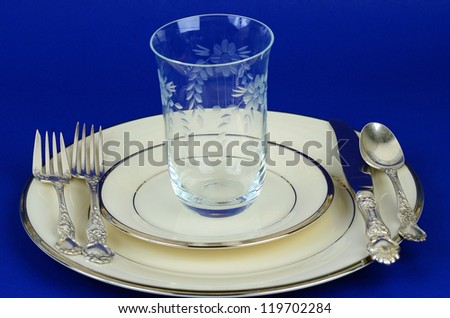Preparation for setting dinner table with fine china, silver and elegant crystal at special occasions.  Setting on blue background.