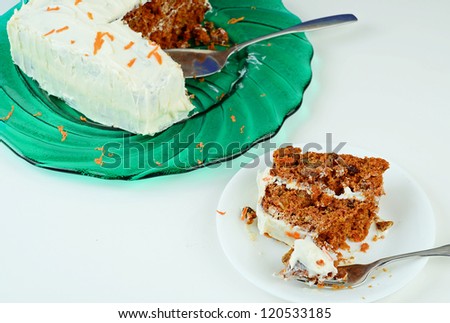 Large slice of carrot cake on saucer in foreground with cake on large green platter in background.