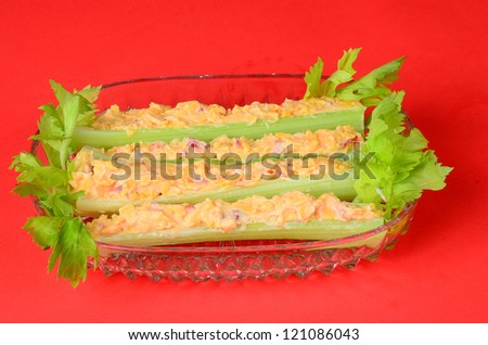 Green leafy celery sticks in clear glass dish stuffed with pimento cheese spread against red background..