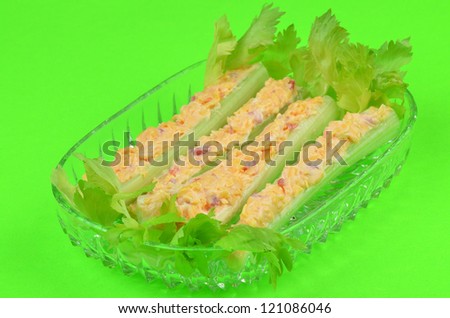 Green leafy celery sticks in clear glass dish stuffed with pimento cheese spread against green Background.