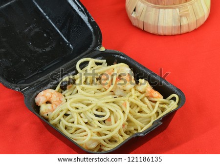 Leftover shrimp pasta in Italian Restaurant take out box on red background with wine bottle.