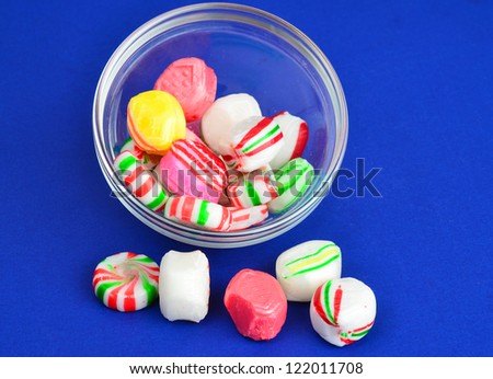 Clear glass bowl of hard candy with several pieces spilled onto foreground.  Colorful image of various imitation flavors on blue background.