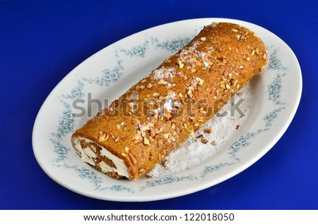 Pumpkin roll with pecans and sprinkled with confectioners sugar on elegant platter against blue background.