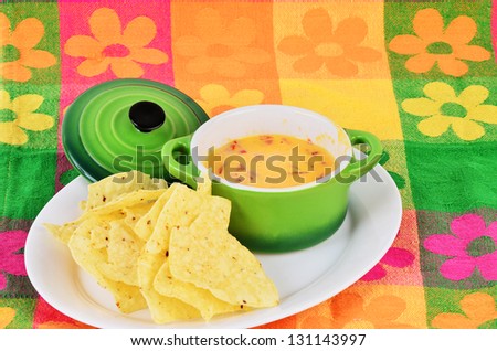 Spicy Chili Con Queso dip in bright green bowl with tortilla chips sitting on colorful place mat.