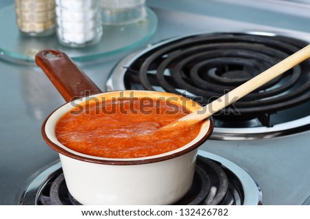 Bubbling hot cream of tomato soup simmering in vintage enamel sauce pan on electric stove.