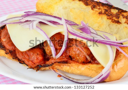 Closeup of juicy meatball sub sandwich on toasted garlic bread with mozzarella cheese and red onions.