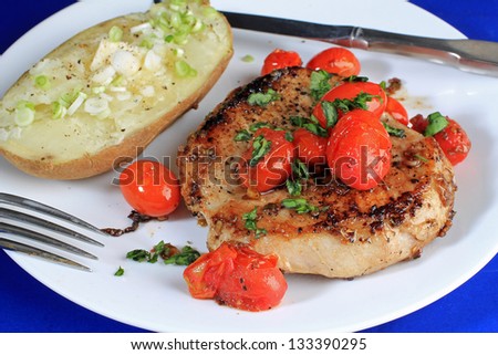 Thick-cut pork chop and tomato skillet saute and served with baked potato.