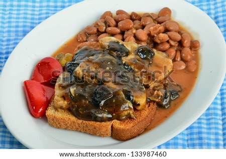 Open-face sandwich with pork tenderloin in mushroom and wine sauce over toast with beans and pickled peppers.