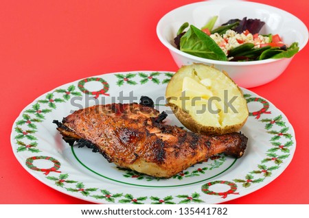 Grilled chicken thigh and leg on Christmas Plate with Baked Potato and Green Garden Salad on bright red background.