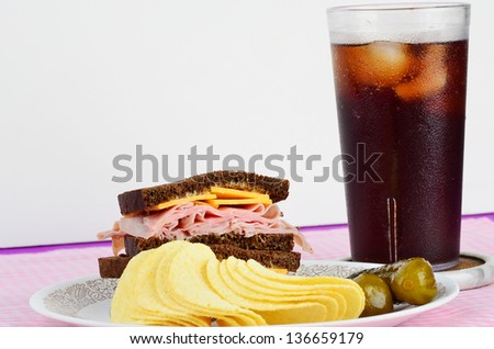 Ham and Cheese Sandwich on Pumpernickel Bread with sweet gherkin and potato chips.  Served with ice cold soft drink.
