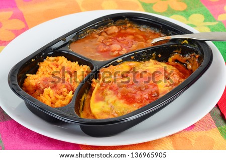 TV Dinner cooked in plastic dish and served on white plate against colorful background.  Beef casserole with Mexican Rice and Borracho Beans.