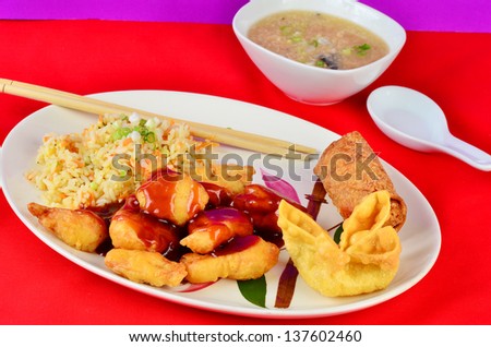 Sweet and sour chicken with fried rice on Oriental Pattern on Plate.  Served with Hot and Sour Soup, Crab Rangoon and Egg Roll against colorful red and purple background.