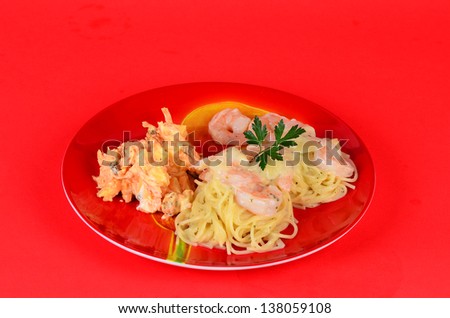 Shrimp Pasta Alfredo on red plate against red background.  Served with carrot, apple and raisin salad