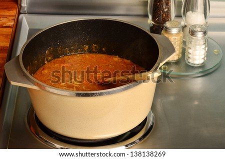 Gumbo bubbling as it cooks in large pot on hot electric stove surrounded by kitchen paraphernalia.
