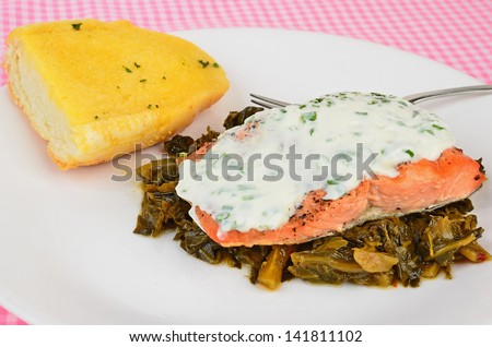 Fresh salmon steak on bed of collard greens covered with creamy dill sauce and served with buttered garlic bread.