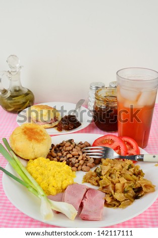 Boiled Cabbage, fried ham, black eyed peas and creamed corn soul food plate with green onions and sliced tomato.  Side plate of buttered biscuit and fig preserves with ice cold glass of sweet tea.