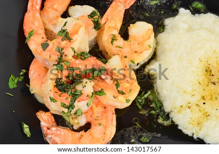 Shrimp Scampi on black plate with grits in garlic butter and garnished with chopped parsley garnish.