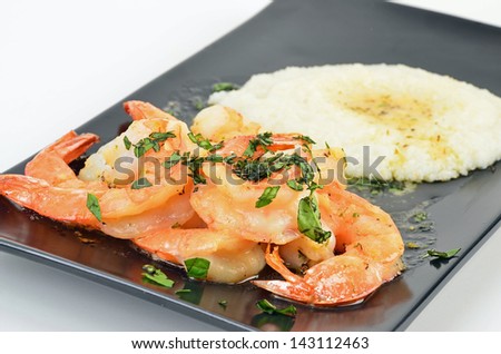Shrimp scampi in sizzling hot garlic butter on black platter with creamed grits in garlic butter and garnished with fresh basil.