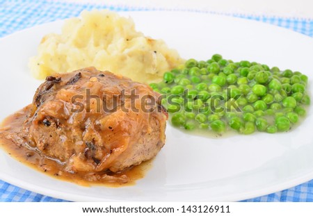 Strong back lighting on Onion gravy over salisbury steak with mashed potatoes and creamed peas on white plate on blue gingham.  Country cooking.