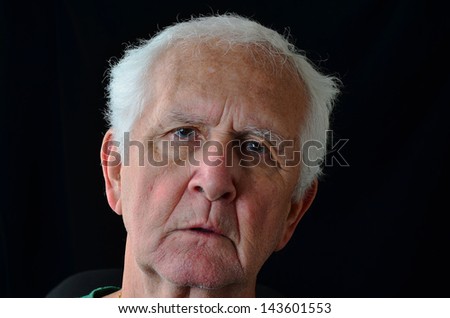 Silver-gray hair and grizzled beard of old man with sad eyes against black background create dark, remorseful image.