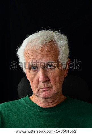 Questioning expression on face of older man with grizzled gray beard and silver gray hair against dark background.