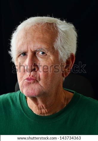 White hair and gray stubble beard on senior man who has lips pursed in expression of distaste or annoyance.