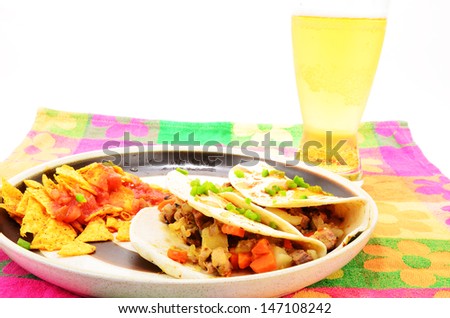 Mexican Burrito Lunch on flour tortilla.  Garnished with diced jalapeno and spicy sauce; served with chips and salsa on brightly colored floral pattern place mat. High Contrast, Horizontal.