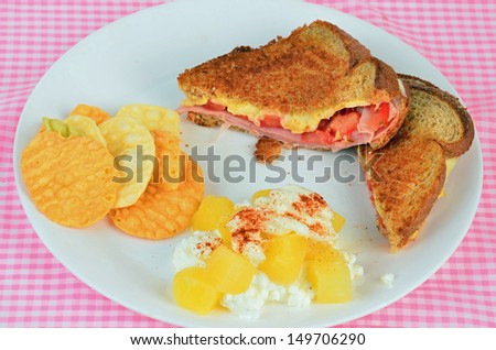 Pineapple and cottage cheese salad with grilled ham and cheese sandwich on white plate with veggie chips.