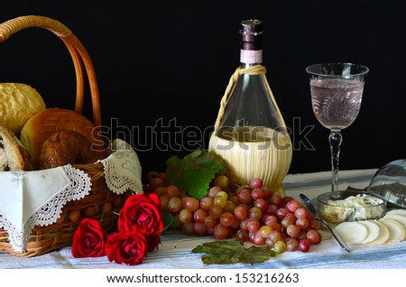 Rembrandt-like still life with bread, grapes, wine and cheese and flowers against dark background.
