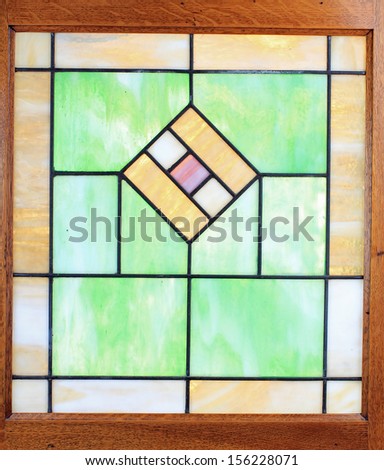 Light shining through antique lead glass window with muted colors -- green, brown; purple; blue; white;