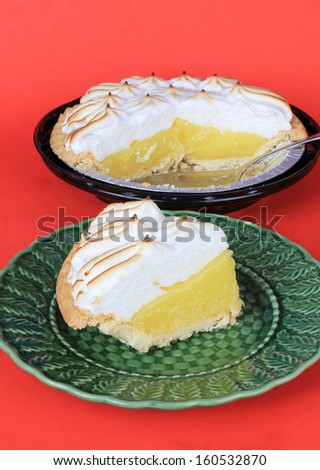 Vertical image of serving of lemon meringue pie on green plate with sliced pie in background.