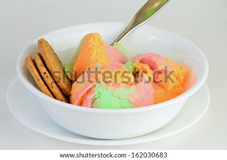 Colorful Rainbow ice cream sherbert of orange, lemon; lime; strawberry flavors in white bowl with cookies.