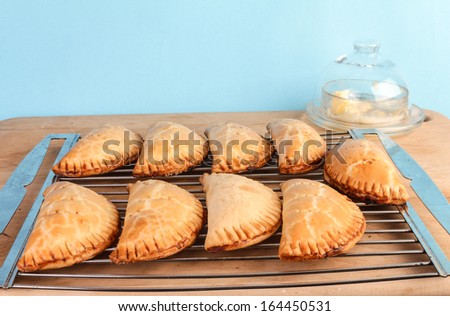 Fresh apricot fried pies cooling on metal rack on wooden cutting board with butter dish in background.