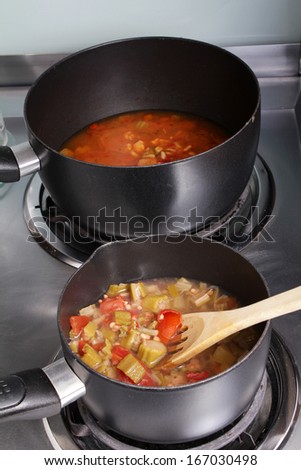 Medium saucepan of Boiling okra and tomato mixture in foreground to be added to larger sauce pan with the Creole style Chicken Gumbo.