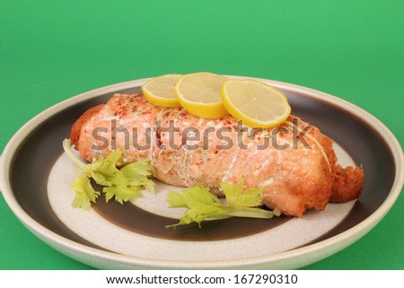 Spicy herbs on rolled pink salmon stuffed with lobster and garnished with lemon and celery against green background
