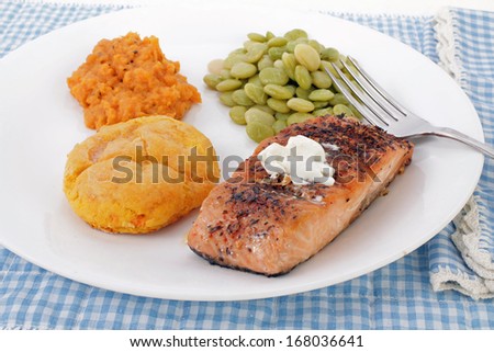 Baked Salmon Steak on white plate with Buttered Sweet Potato biscuit, butter beans and candied yams; strong light from above and behind subject.